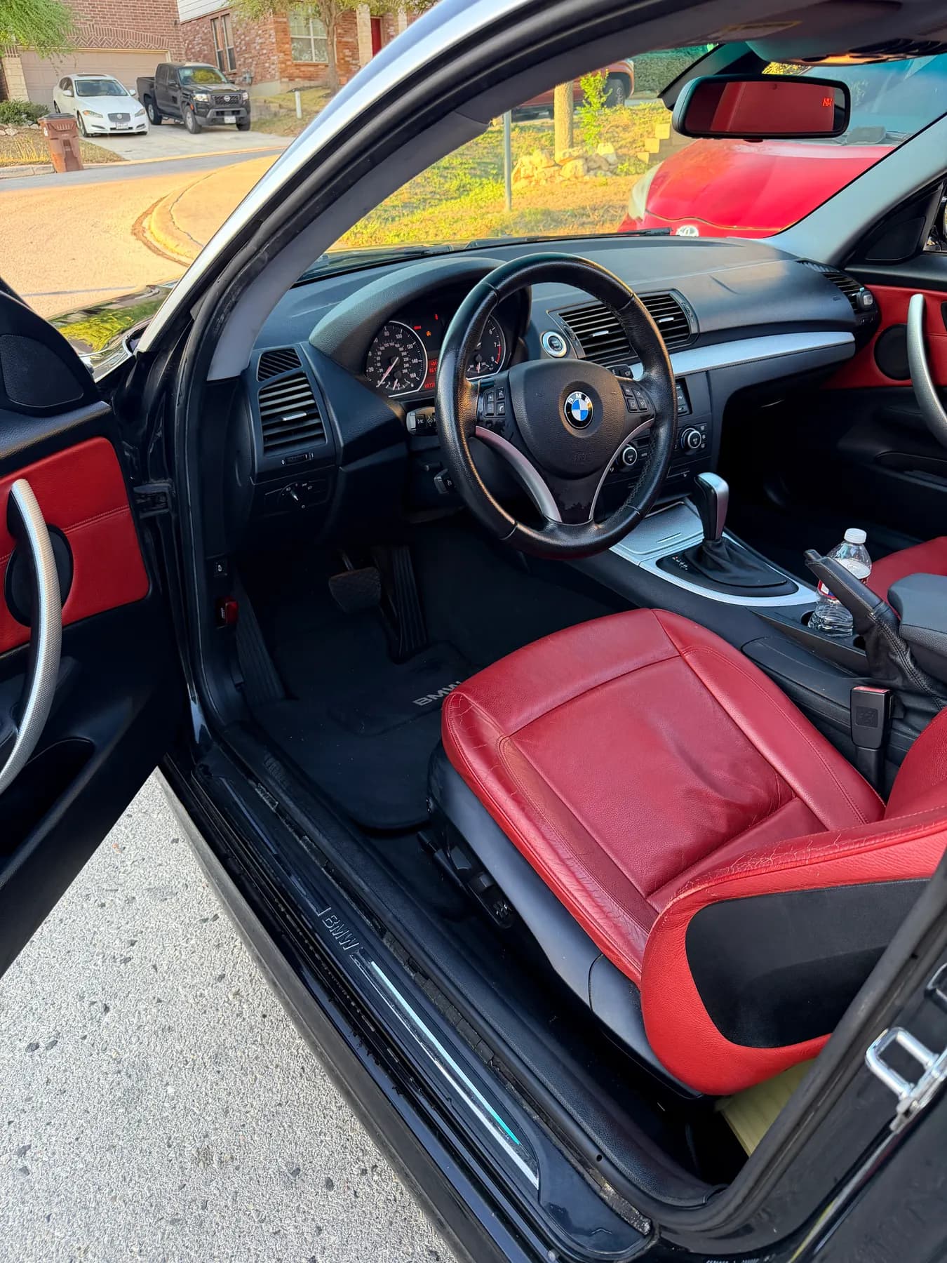 The BMW's driver door standing open on a red leather interior, dashboard and steering wheel wiped down.