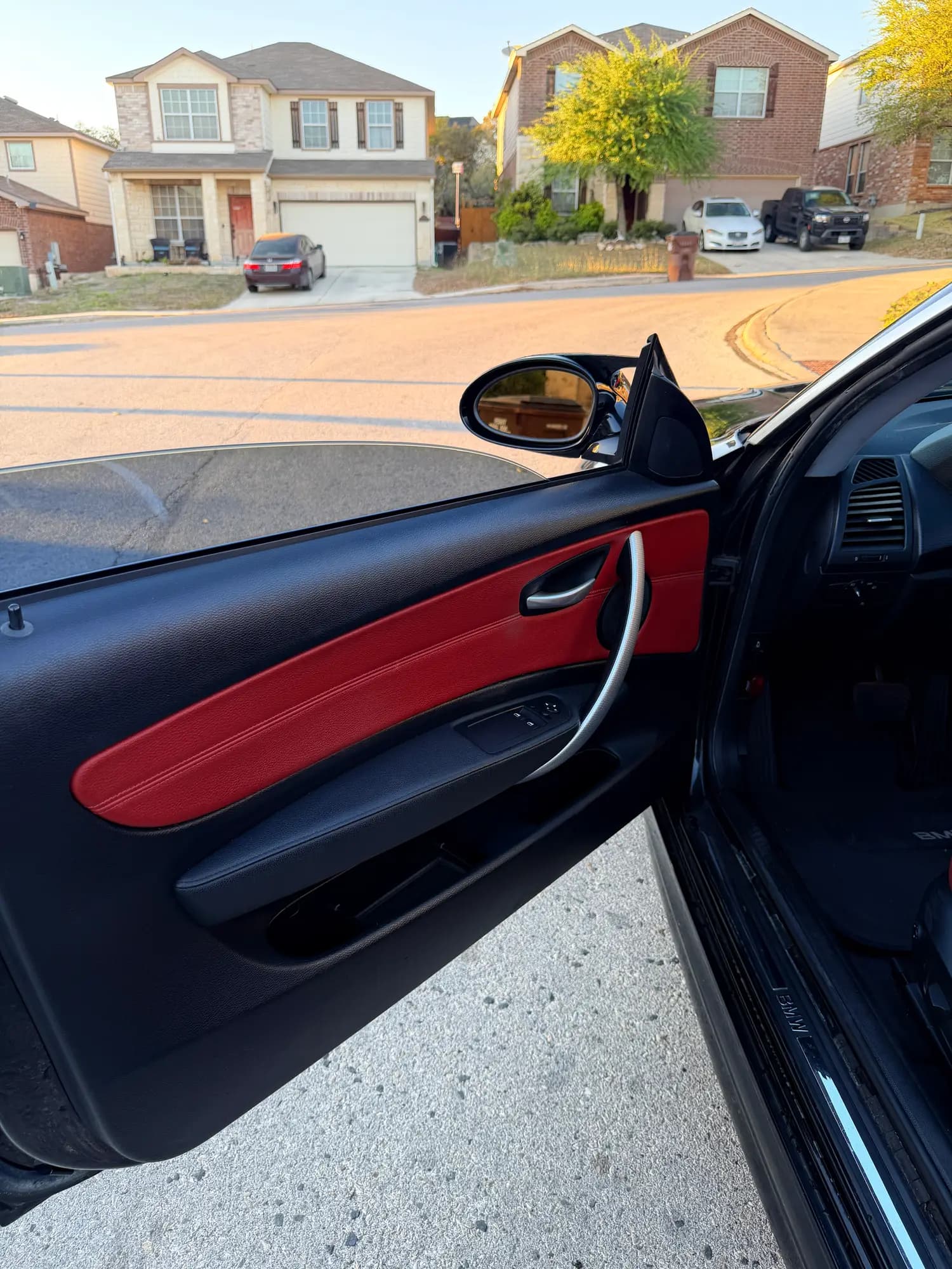 Close view of the BMW's driver door card, red leather insert, black trim, and the wing mirror beyond.
