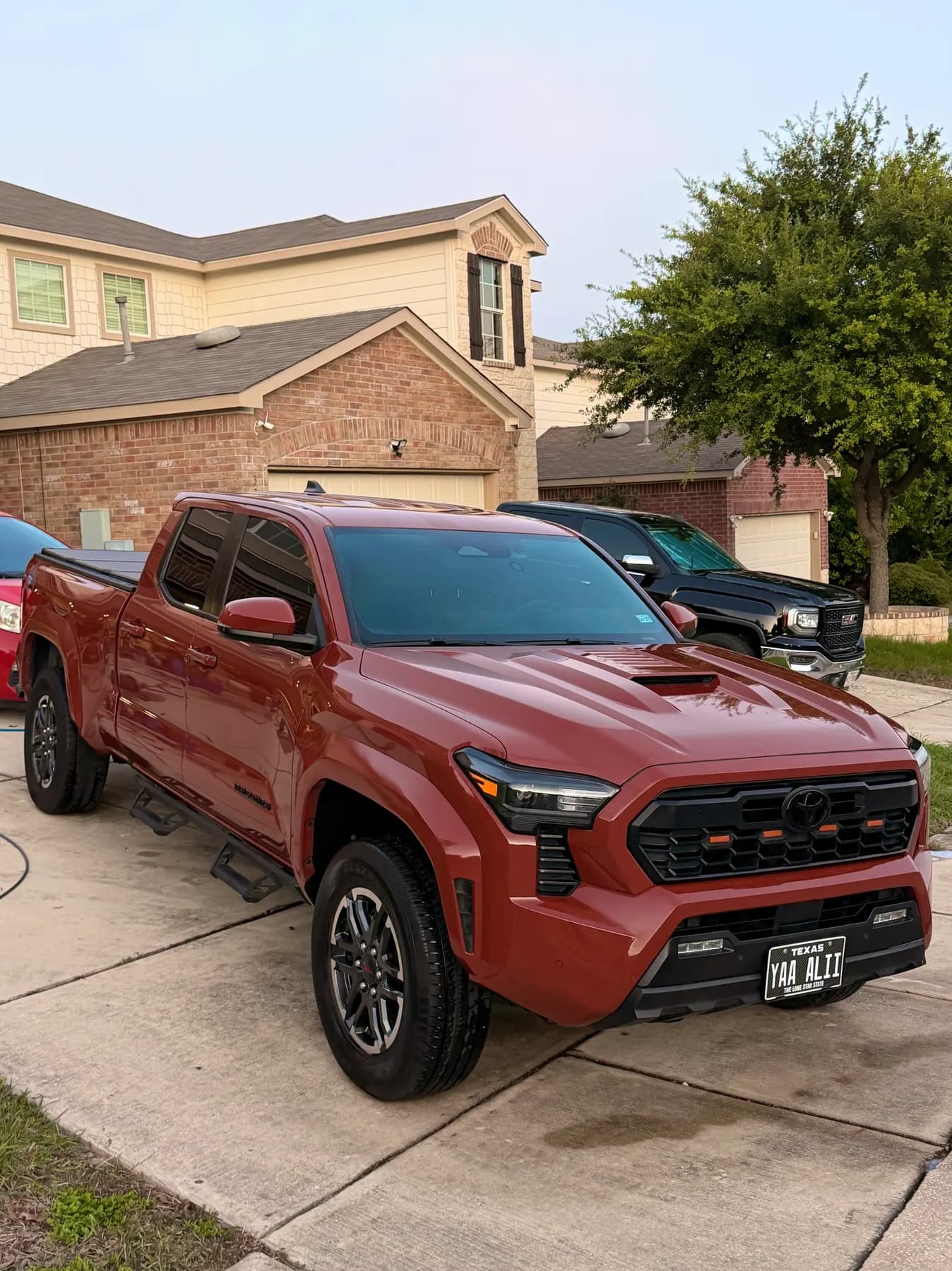 A copper-red Toyota Tacoma on a driveway after a wash, paint glossy in flat evening light.
